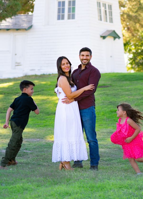 Family of four with playful children by a white farmhouse