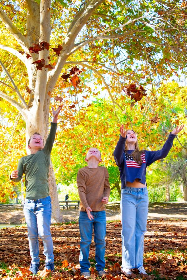 Three kids joyfully throwing autumn leaves in the air